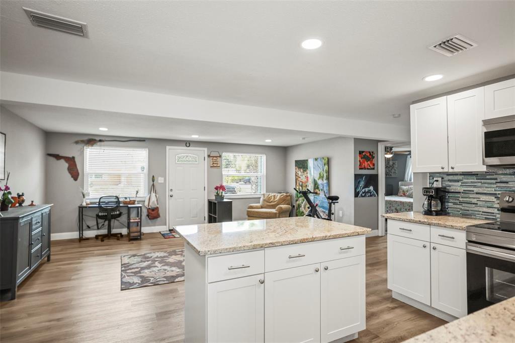 A kitchen with a granite-topped island and white cabinets opens into a living area — 4704 KOALA DRIVE, HOLIDAY, FL