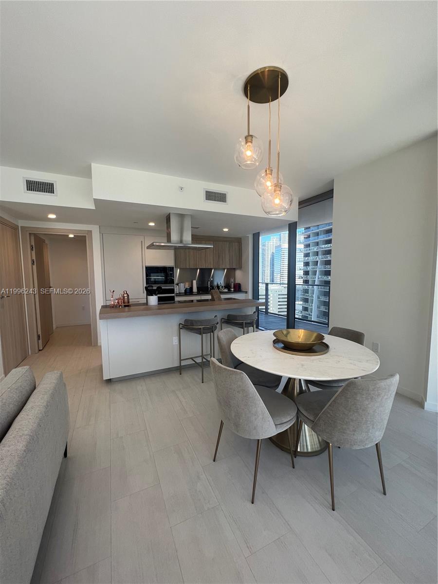 A modern kitchen and dining area with a marble table, bar seating, and city views — 1000 Brickell Plaza # 2701, Miami FL 33131, MIAMI, FL