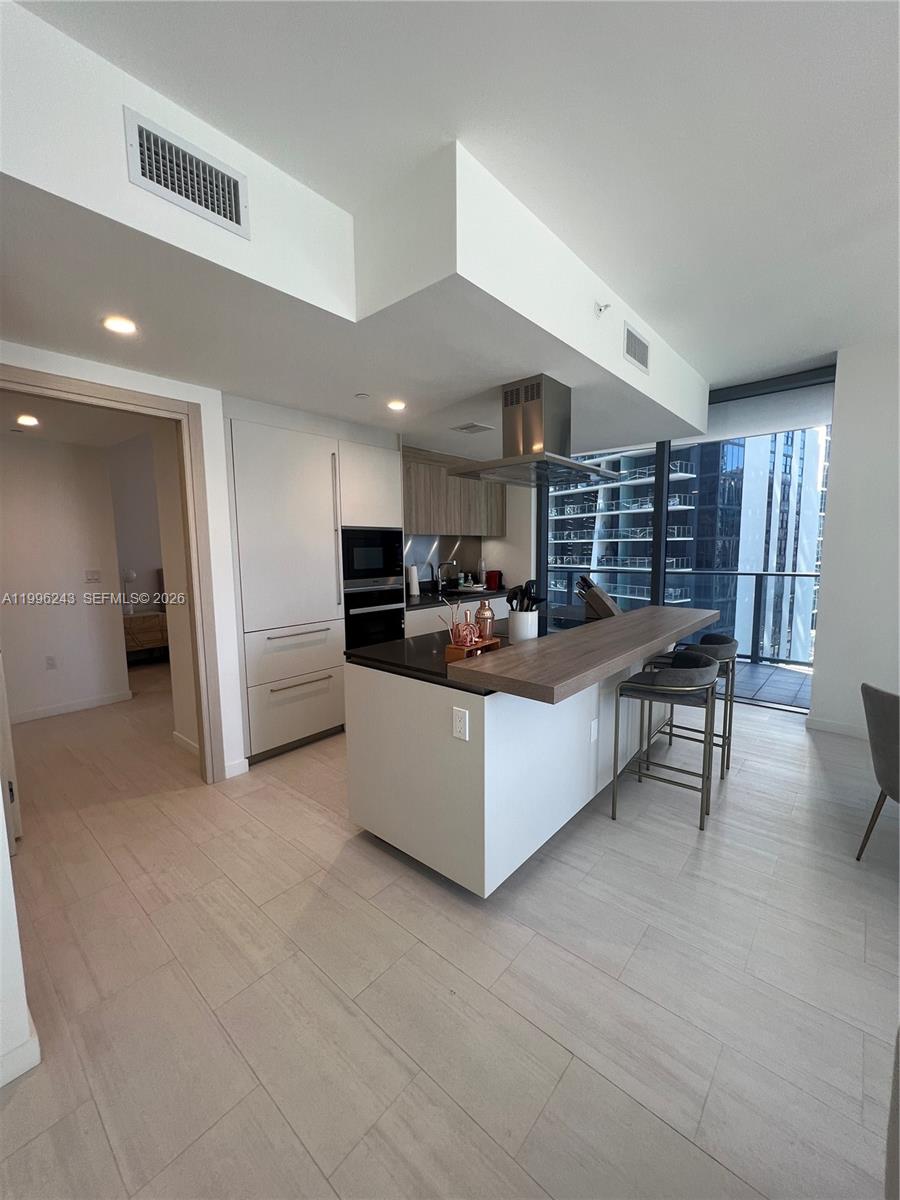 A modern kitchen features a central island with a wood breakfast bar and stainless appliances — 1000 Brickell Plaza # 2701, Miami FL 33131, MIAMI, FL
