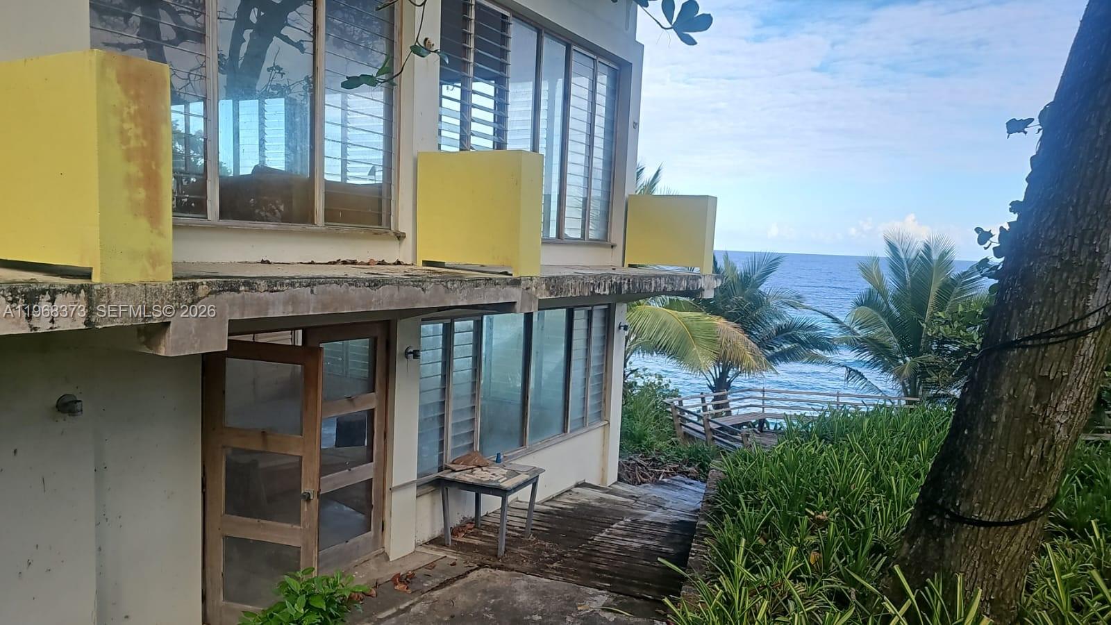 A two-story building with yellow balcony railings overlooks the ocean from a grassy slope — 00 Oracabessa, St. Mary, NA, NA