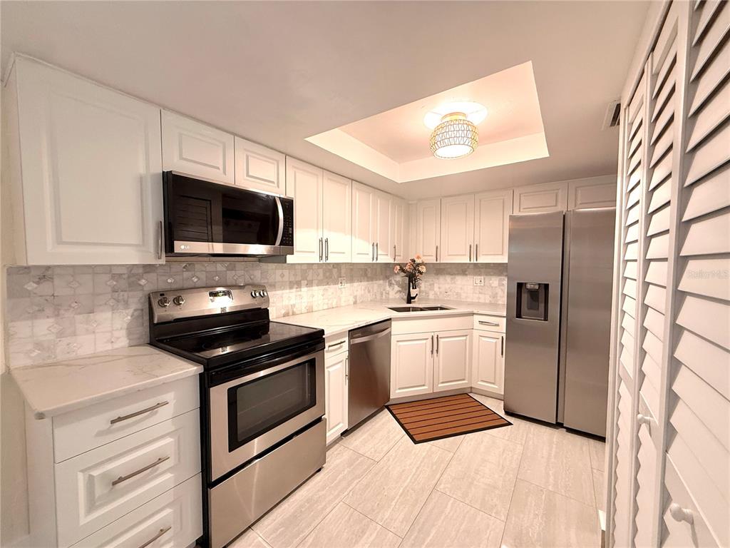 A kitchen features white cabinets, stainless steel appliances, a tiled backsplash, and light-colored flooring — 2363 FLANDERS WAY UNIT D, SAFETY HARBOR, FL