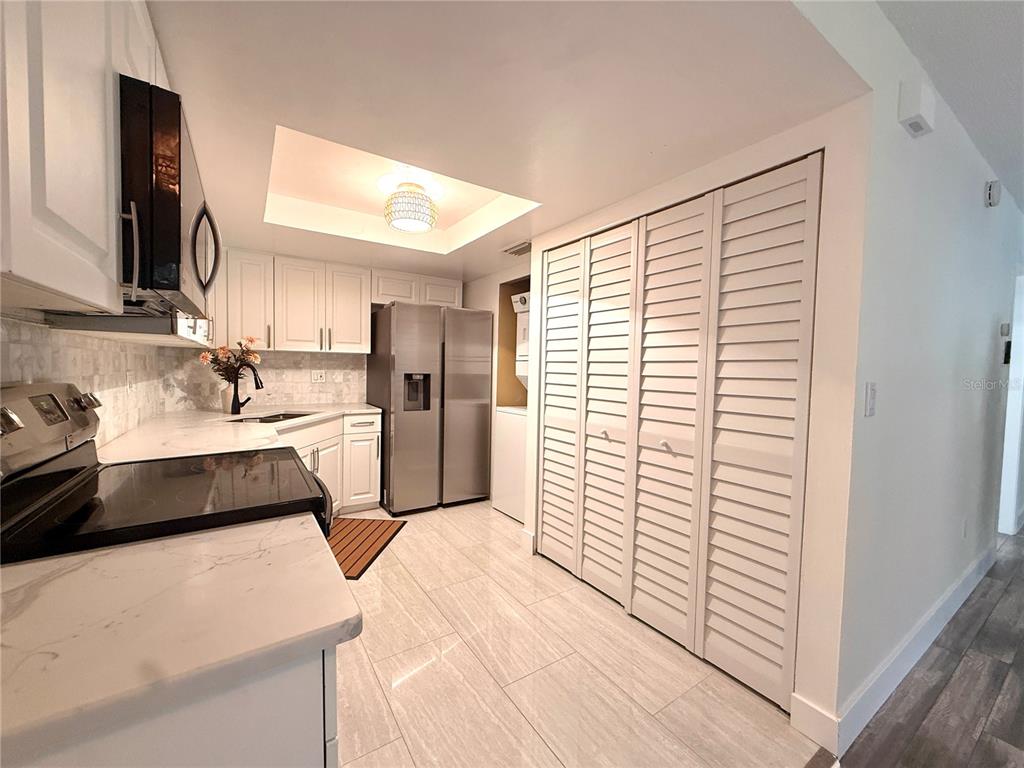 A kitchen features white cabinetry, stainless steel appliances, marble-look countertops, and louvered closet doors — 2363 FLANDERS WAY UNIT D, SAFETY HARBOR, FL