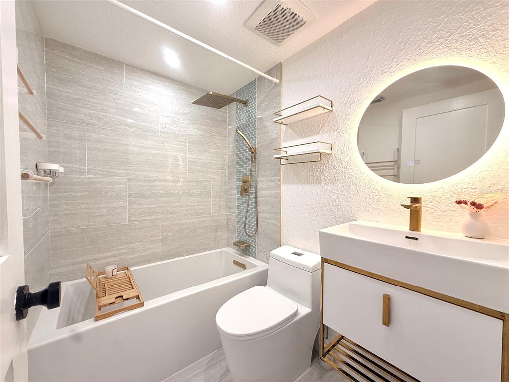 A modern bathroom features a white vanity, a round LED mirror, and a tiled tub — 2363 FLANDERS WAY UNIT D, SAFETY HARBOR, FL