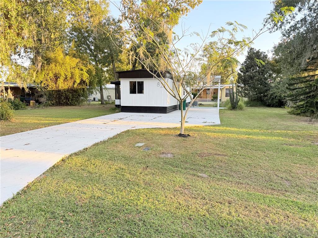 A white mobile home with a dark roof sits on a lot with a concrete driveway — 82 N BOBWHITE ROAD, WILDWOOD, FL