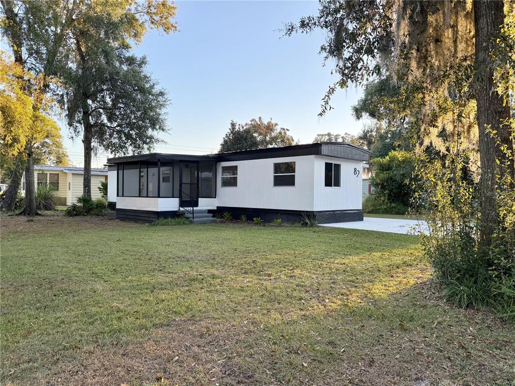 A white manufactured home with a black trim and a screened-in front porch — 82 N BOBWHITE ROAD, WILDWOOD, FL