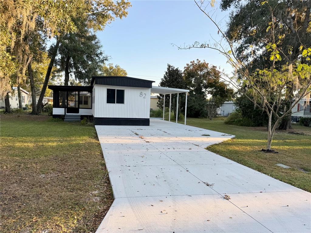 A white manufactured home with black trim features a concrete driveway and a carport — 82 N BOBWHITE ROAD, WILDWOOD, FL