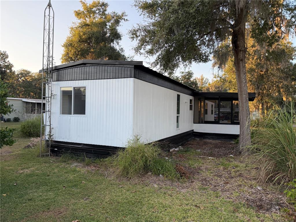 A white mobile home with black trim and a screened-in porch sits on a grassy lot — 82 N BOBWHITE ROAD, WILDWOOD, FL