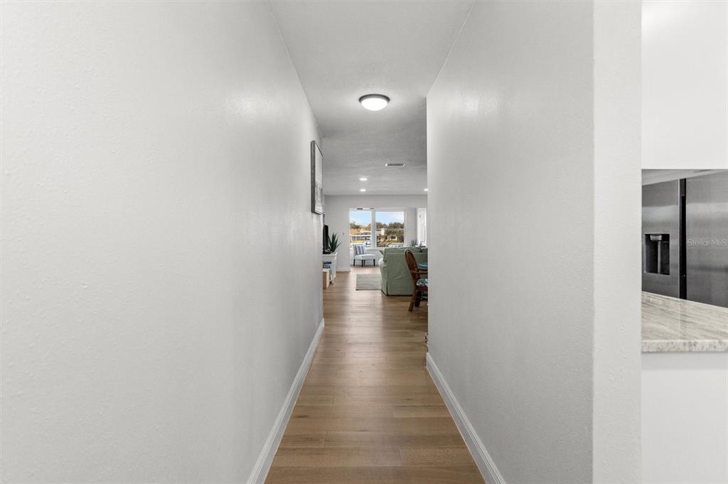 A hallway with light wood flooring leads to an open living area with a view — 5955 30TH AVENUE S UNIT 202, GULFPORT, FL
