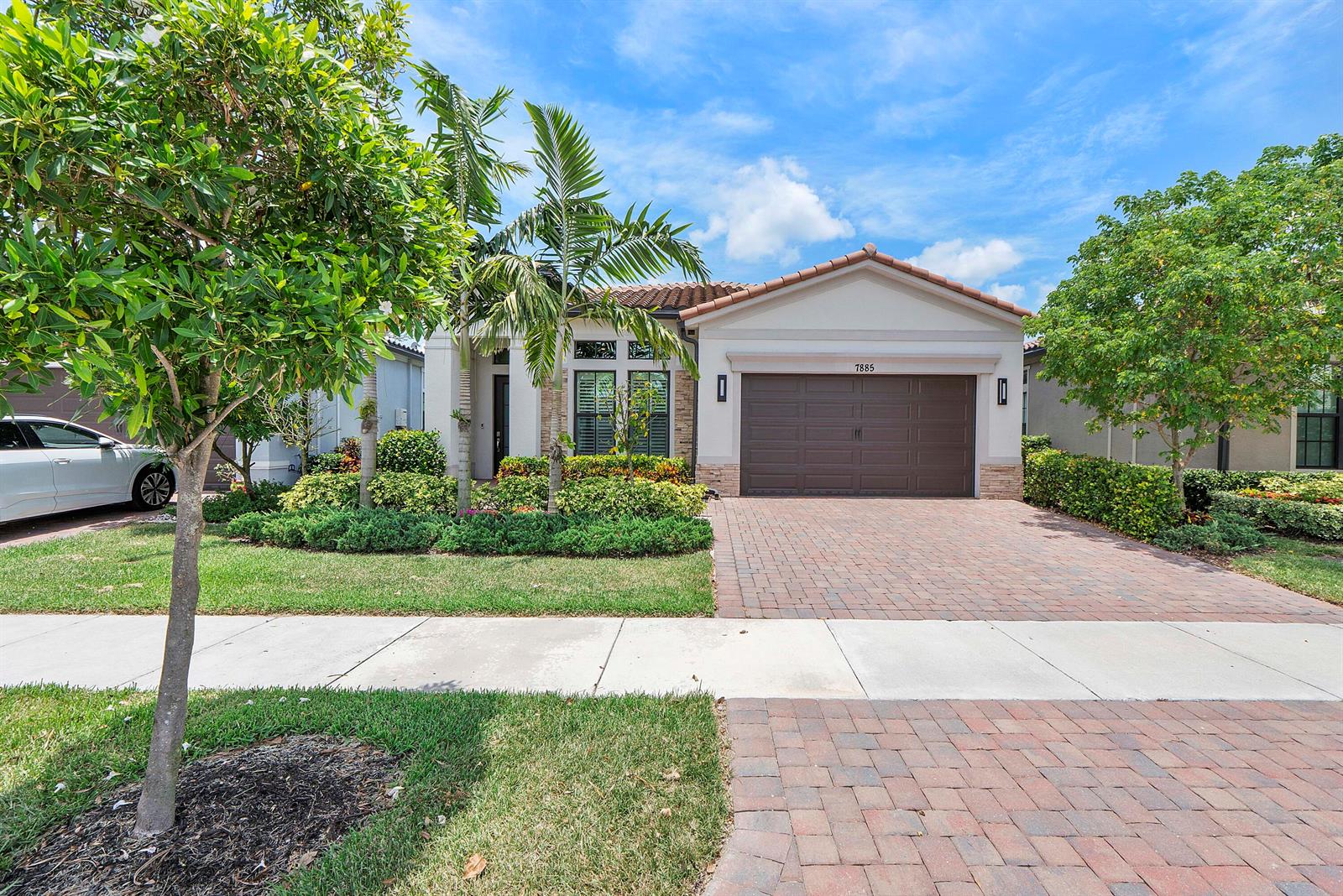 A single-story house with a brown garage door, brick driveway, and palm trees in front — 7885 Ironwood Way, Parkland FL 33067, PARKLAND, FL