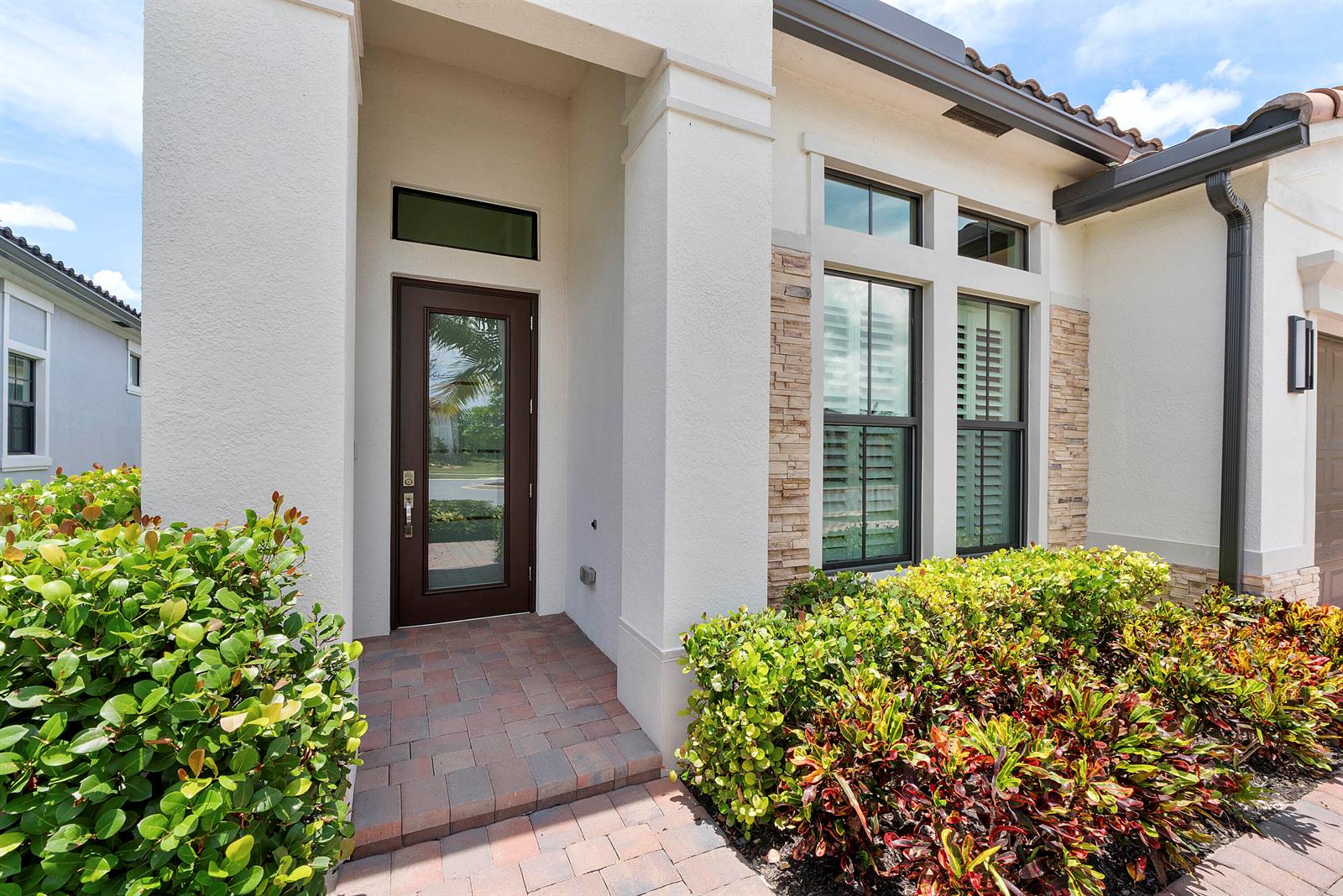 The front entrance features a brown glass-paneled door, stone accents, and a brick walkway — 7885 Ironwood Way, Parkland FL 33067, PARKLAND, FL
