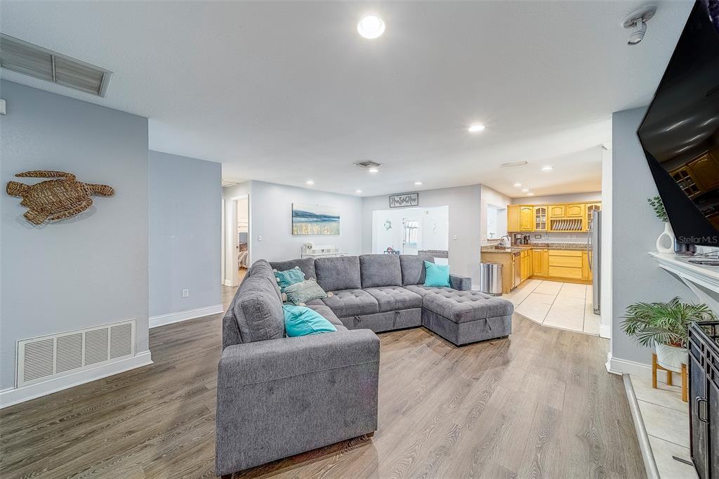 A grey sectional sofa sits in a living room with wood-look flooring and an open kitchen — 14414 91ST AVENUE, SEMINOLE, FL