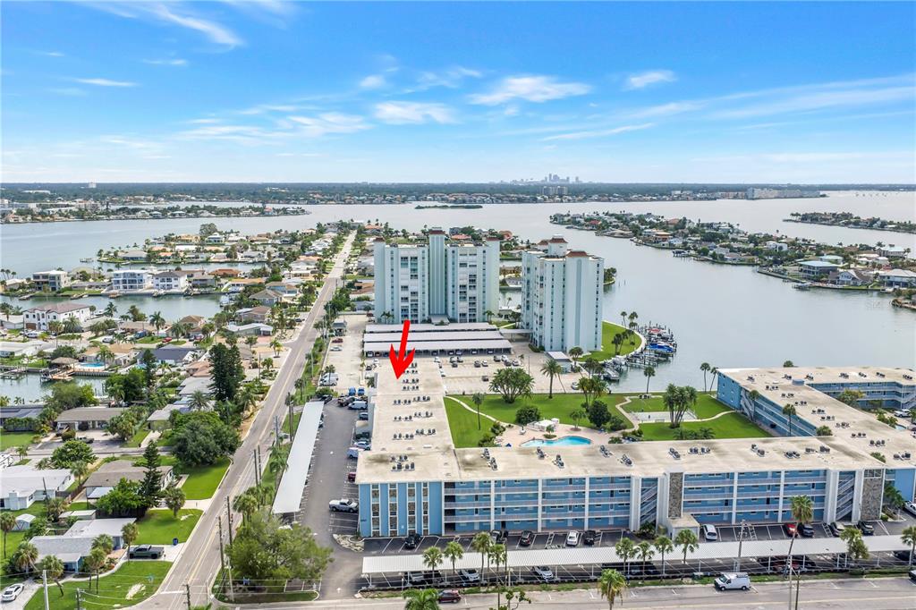An aerial view shows a multi-story blue apartment complex with a red arrow pointing down — 300 64TH AVENUE UNIT 117, ST PETE BEACH, FL