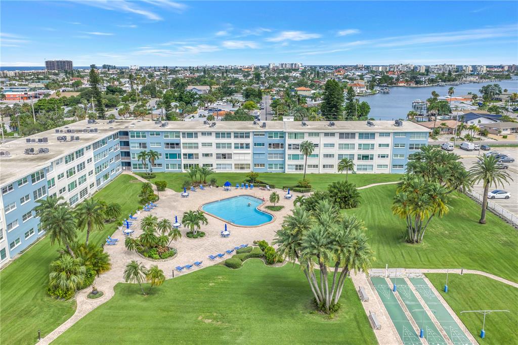 An aerial view of a multi-story apartment building with a swimming pool and shuffleboard courts — 300 64TH AVENUE UNIT 117, ST PETE BEACH, FL