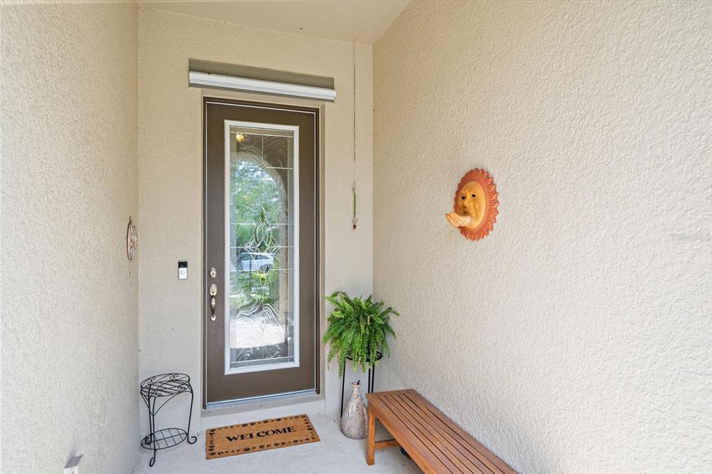 A covered entryway features a brown front door, a wooden bench, and a sun wall decoration — 12940 BLISS LOOP, BRADENTON, FL