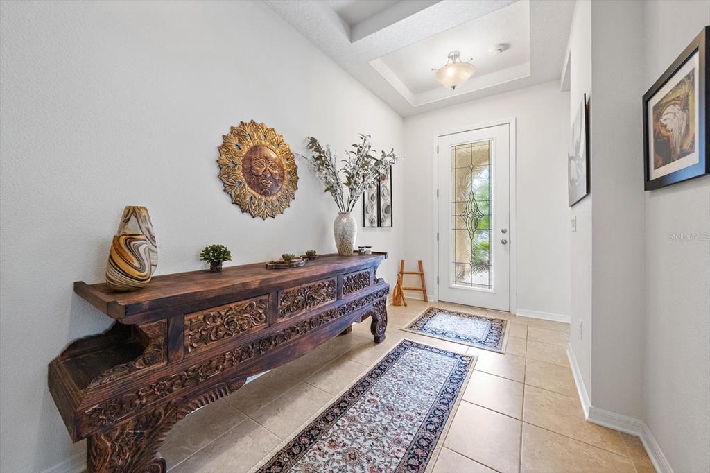 An entryway features a carved wooden console table, a sun wall hanging, and tiled flooring — 12940 BLISS LOOP, BRADENTON, FL
