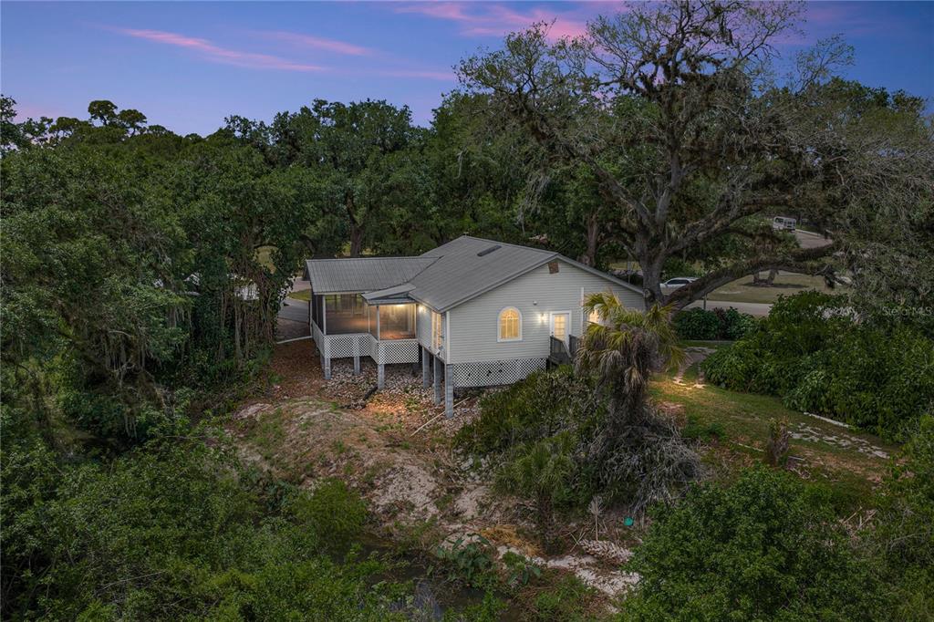 An elevated house with a metal roof and screened porch sits among trees near water — 975 CALOOSA ESTATES DRIVE, LABELLE, FL