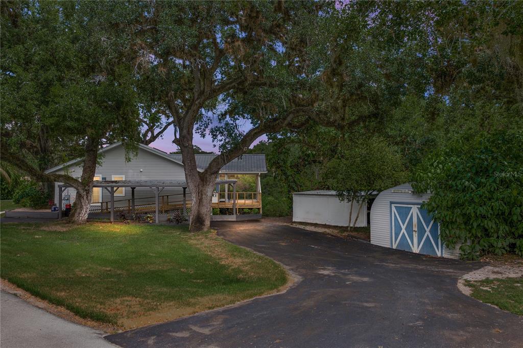 A gray house with a wooden deck and a driveway featuring two storage sheds — 975 CALOOSA ESTATES DRIVE, LABELLE, FL