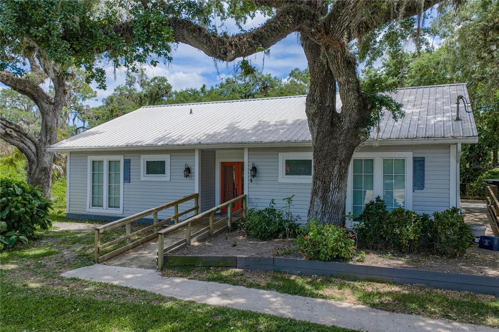 A single-story house with light gray siding, a metal roof, and a wooden wheelchair ramp — 975 CALOOSA ESTATES DRIVE, LABELLE, FL