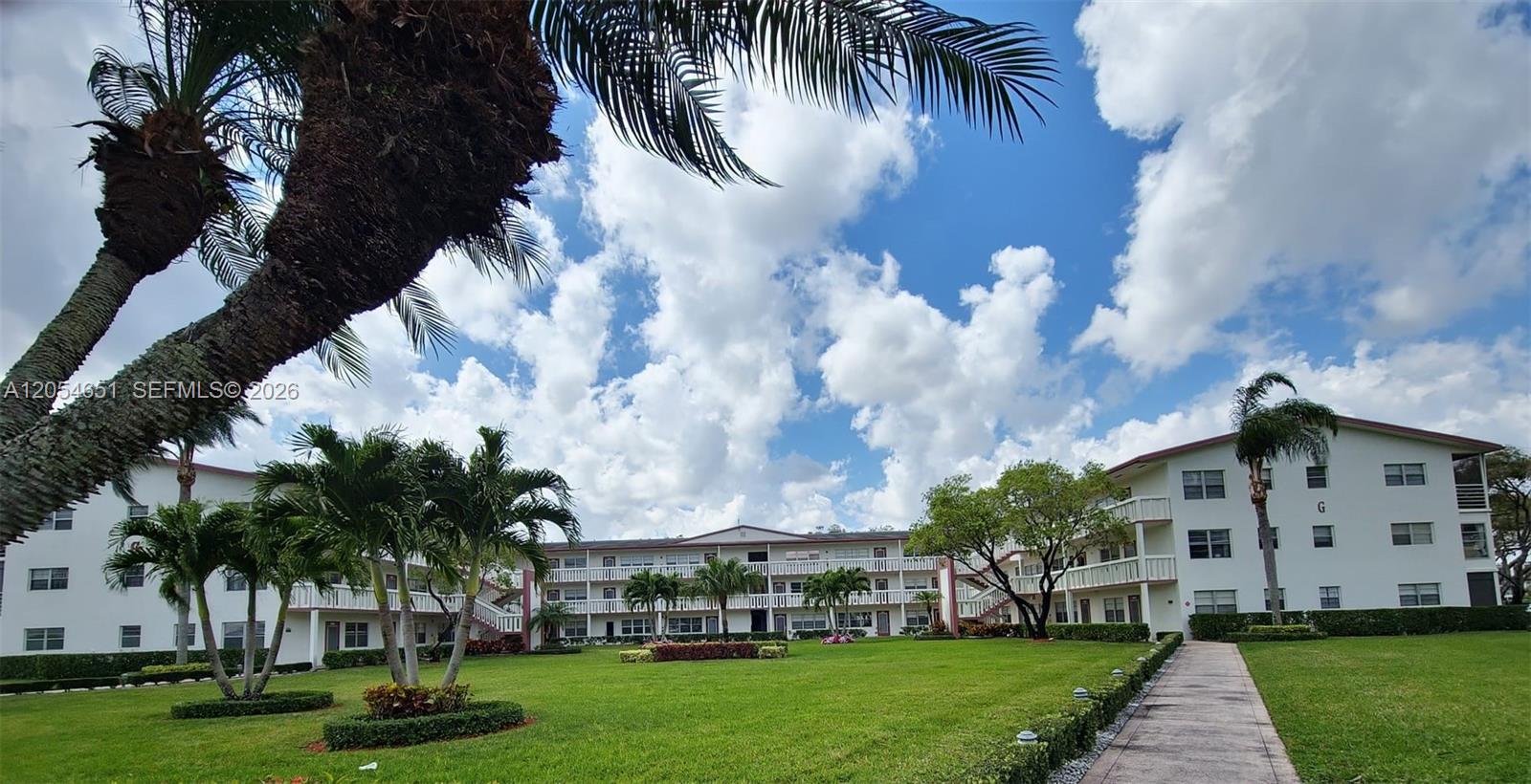 A multi-story apartment complex features white exterior walls, balconies, and a landscaped lawn — 285 Fanshaw G # G, Boca Raton FL 33434, BOCA RATON, FL