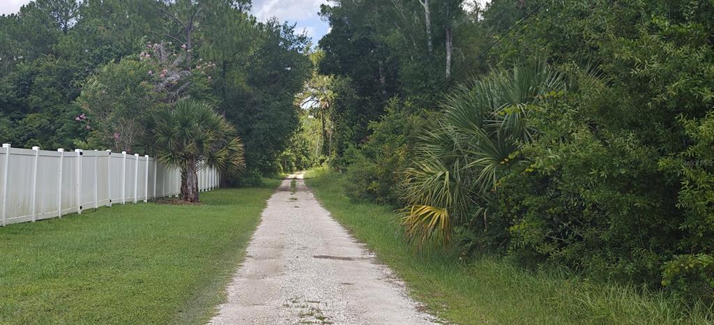 A gravel path leads through a wooded area past a white vinyl fence — 8401 AMELIA TRAIL, KISSIMMEE, FL