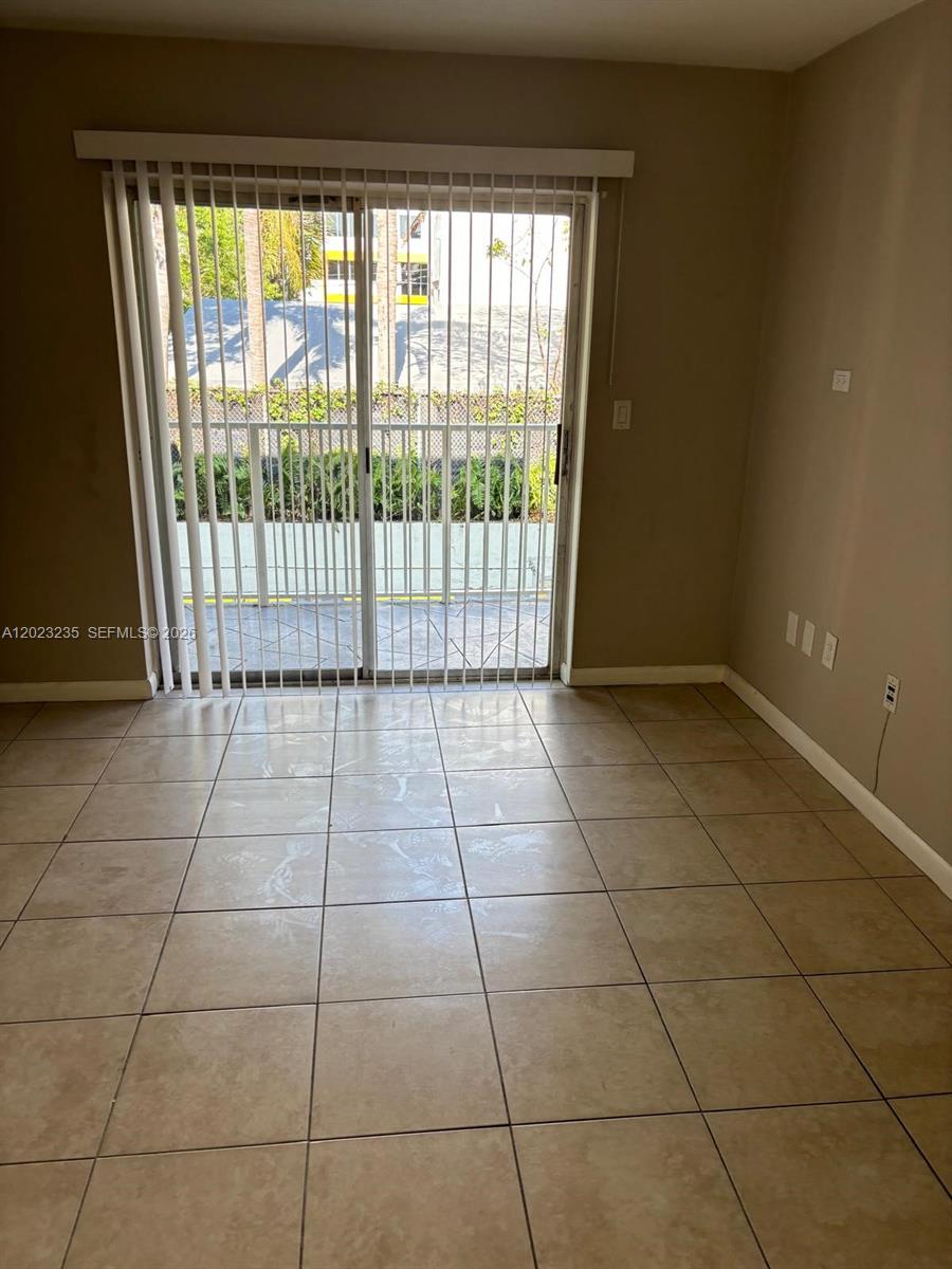 An empty room features beige tile flooring and a sliding glass door leading outside — 3050 S Dixie Hwy # 203, Miami FL 33133, MIAMI, FL