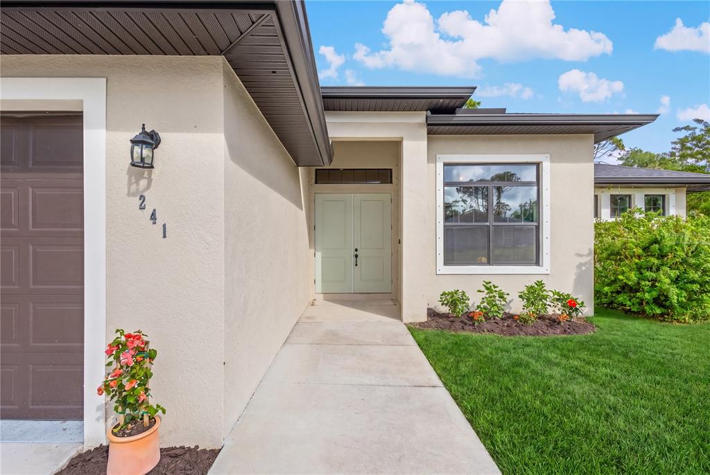 The exterior of a house features a light-colored facade, double front doors, and a walkway — 241 HOFFER STREET, PORT CHARLOTTE, FL
