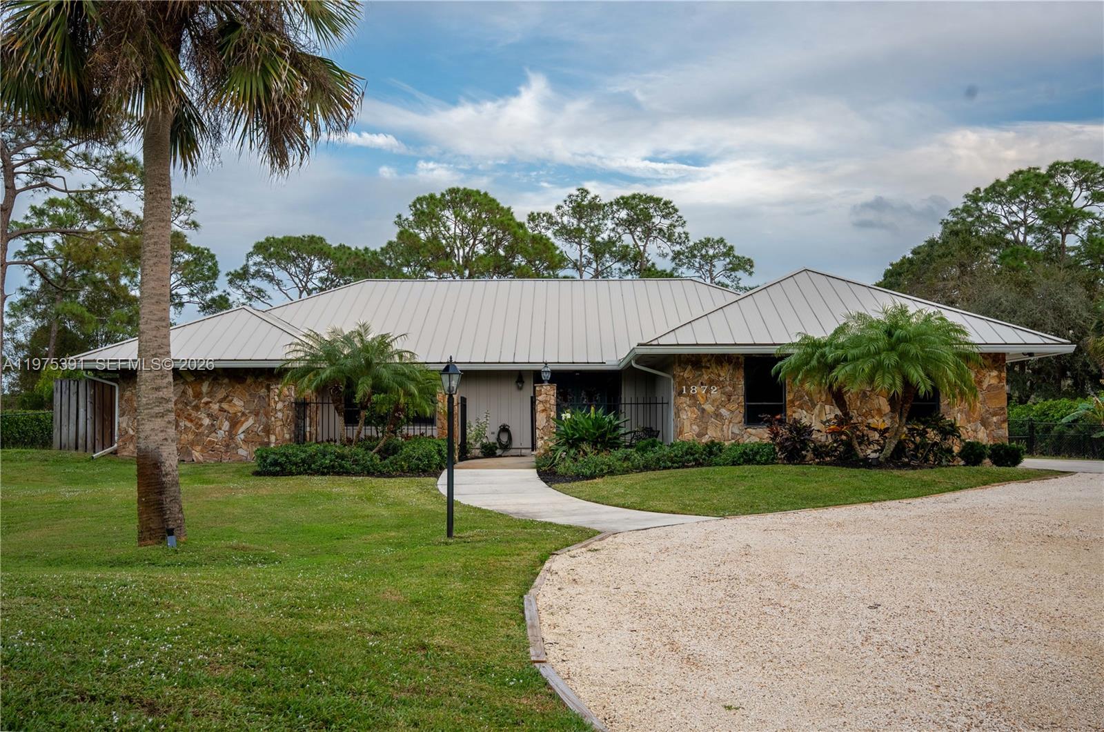 A single-story house with a stone facade, metal roof, and a gravel driveway — 1872 SE Colony Way, Jupiter FL 33478, JUPITER, FL