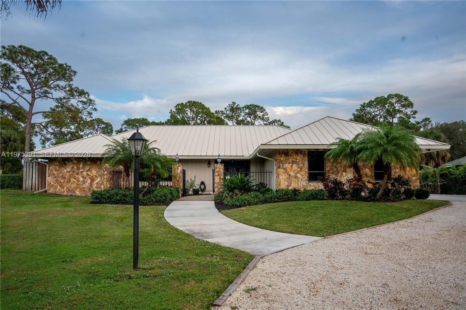 A single-story house with a stone facade, metal roof, and a curved concrete walkway — 1872 SE Colony Way, Jupiter FL 33478, JUPITER, FL