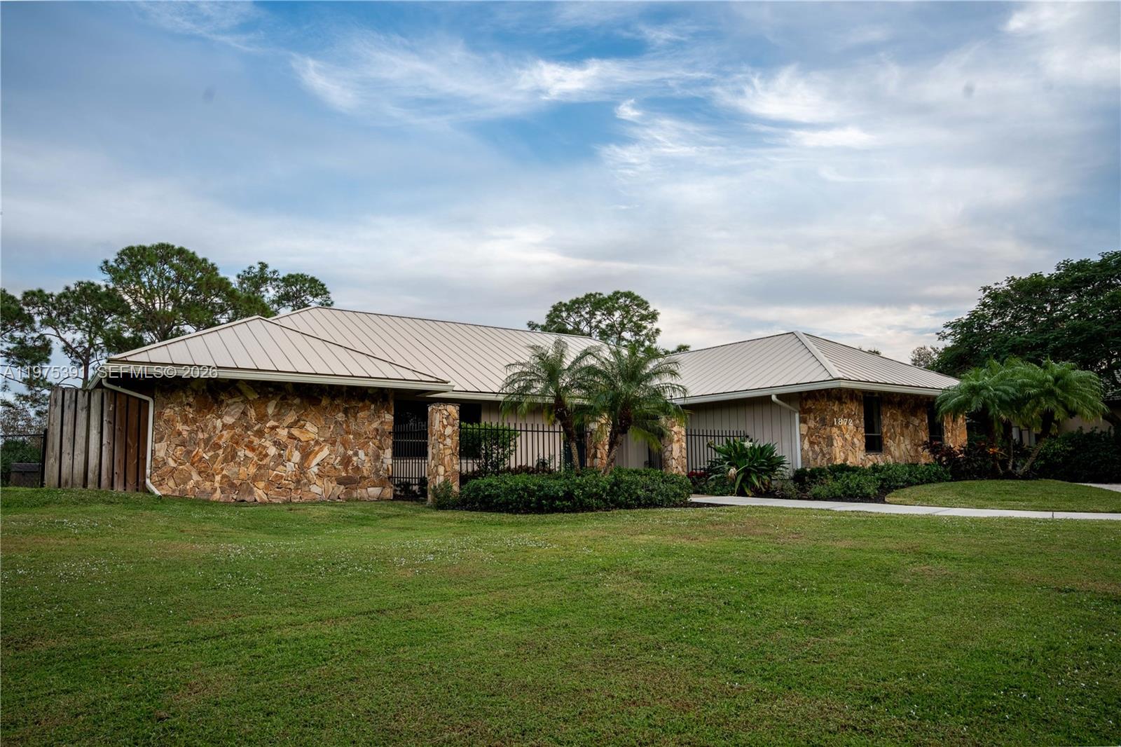 A single-story house with a stone facade and a metal roof sits on a lawn — 1872 SE Colony Way, Jupiter FL 33478, JUPITER, FL