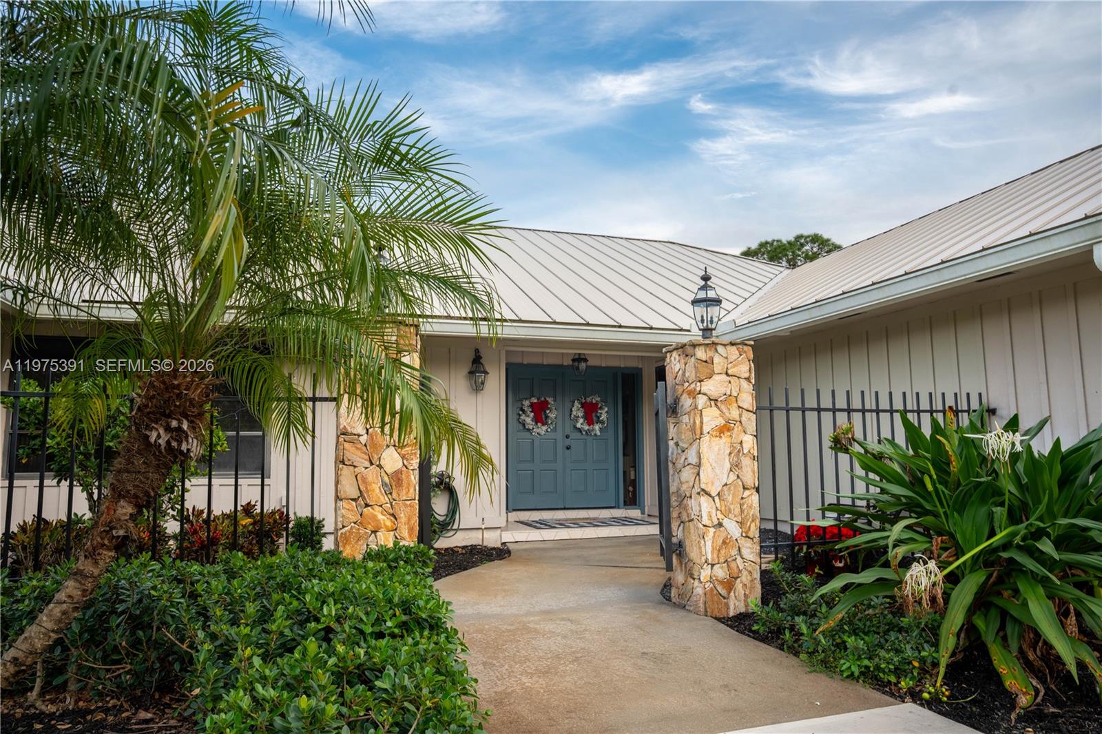 A stone-columned entryway leads to a blue double door with wreaths under a metal roof — 1872 SE Colony Way, Jupiter FL 33478, JUPITER, FL