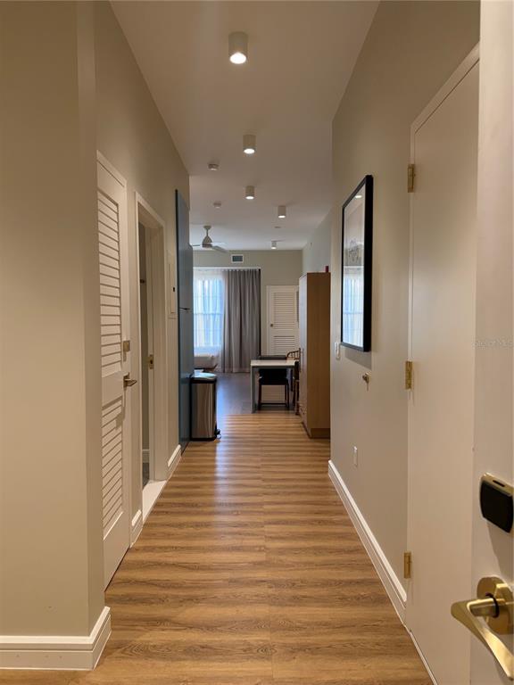 A hallway with light wood-look flooring leads toward a dining area with a window — 3151 SUNSET WALK DRIVE UNIT 416, KISSIMMEE, FL