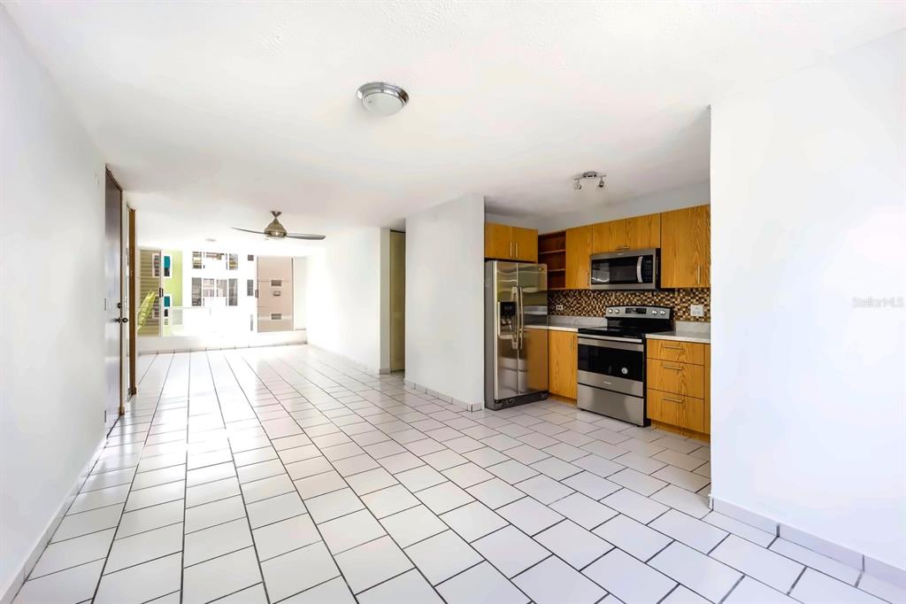 A kitchen with wood cabinets and stainless steel appliances opens to a tiled living area — Alturas de Piedras Blanca UNITS D-202, GUAYNABO, PR