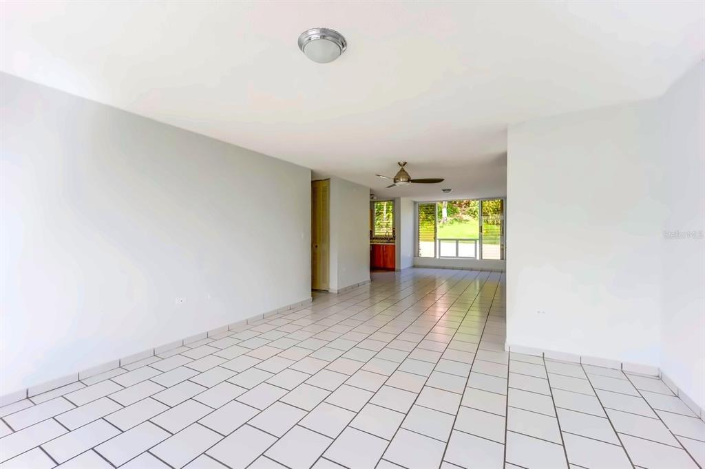 An empty living area with white tiled floors, a ceiling fan, and a distant kitchen — Alturas de Piedras Blanca UNITS D-202, GUAYNABO, PR