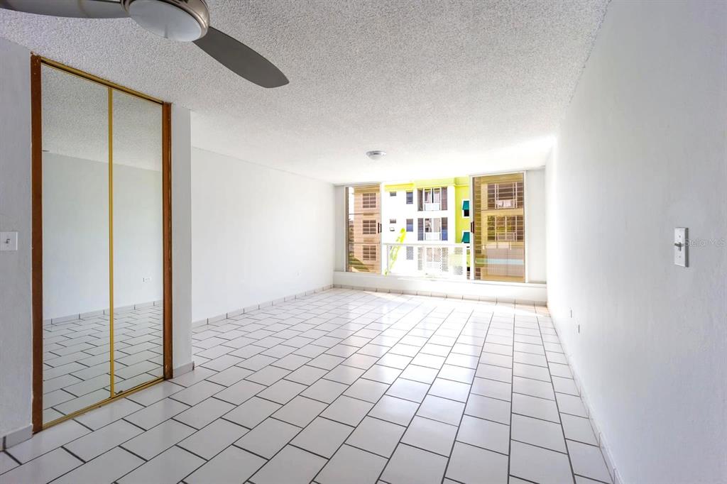 An empty room features white tile flooring, a mirrored closet, and a large window view — Alturas de Piedras Blanca UNITS D-202, GUAYNABO, PR