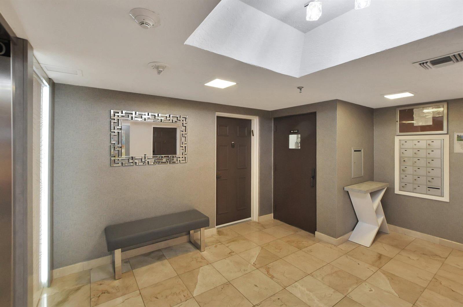 A lobby area with a gray bench, a decorative mirror, mailboxes, and tiled flooring — 7194 Promenade Drive # 102, Boca Raton FL 33433, BOCA RATON, FL