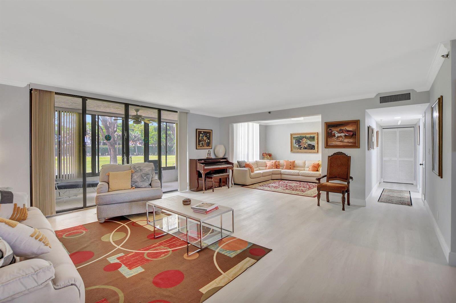 A spacious living room features light wood flooring, a piano, and large sliding glass doors — 7194 Promenade Drive # 102, Boca Raton FL 33433, BOCA RATON, FL