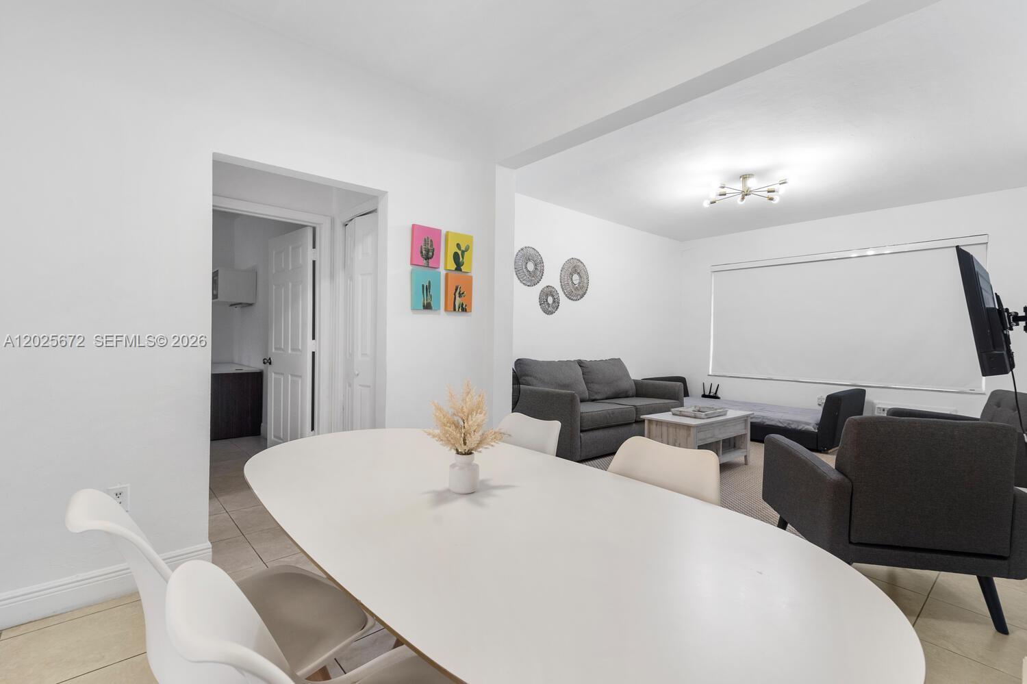 A dining area with a white table leads into a living room with gray furniture — 301 86th St # 1, Miami Beach FL 33141, MIAMI BEACH, FL