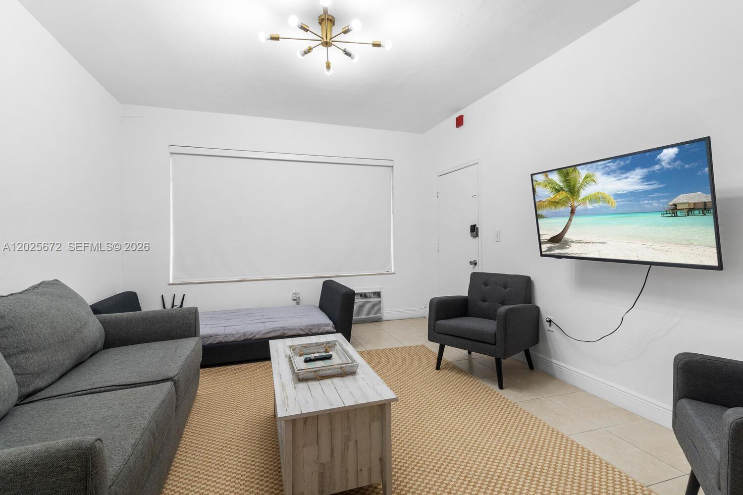 A living room features a gray sofa, two armchairs, a daybed, and a wall-mounted television — 301 86th St # 1, Miami Beach FL 33141, MIAMI BEACH, FL