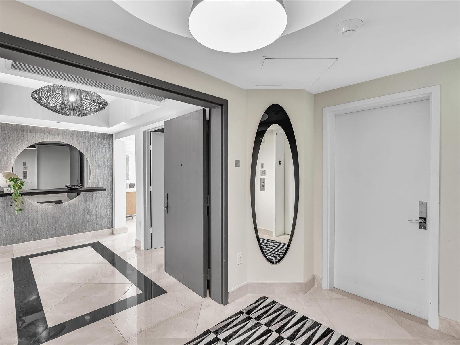 A modern entryway features a gray door, an oval mirror, and a patterned area rug — 1600 S Ocean Boulevard, Pompano Beach FL 33062, POMPANO BEACH, FL