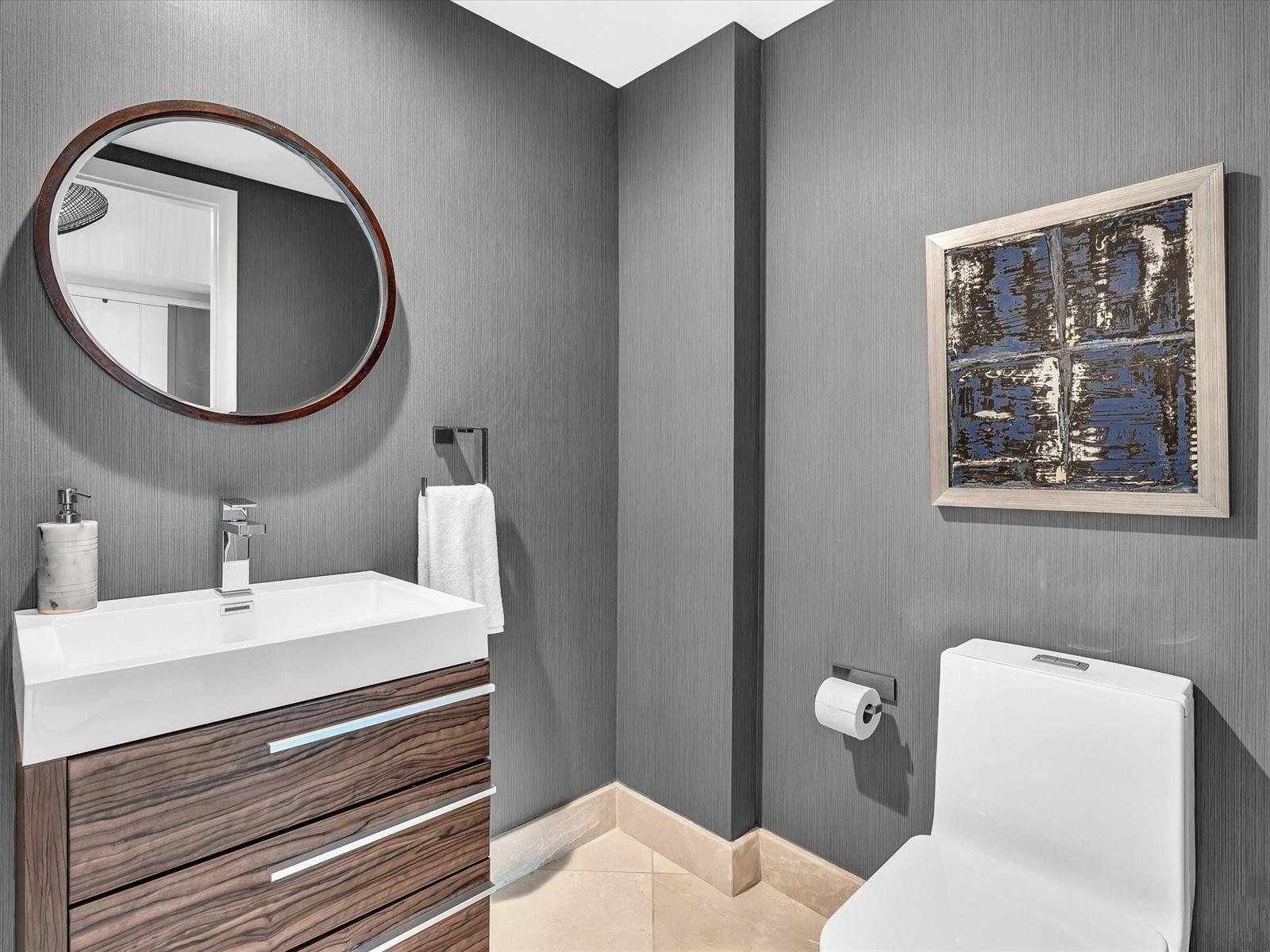 A modern powder room features dark textured wallpaper, a wood vanity, and a round mirror — 1600 S Ocean Boulevard, Pompano Beach FL 33062, POMPANO BEACH, FL