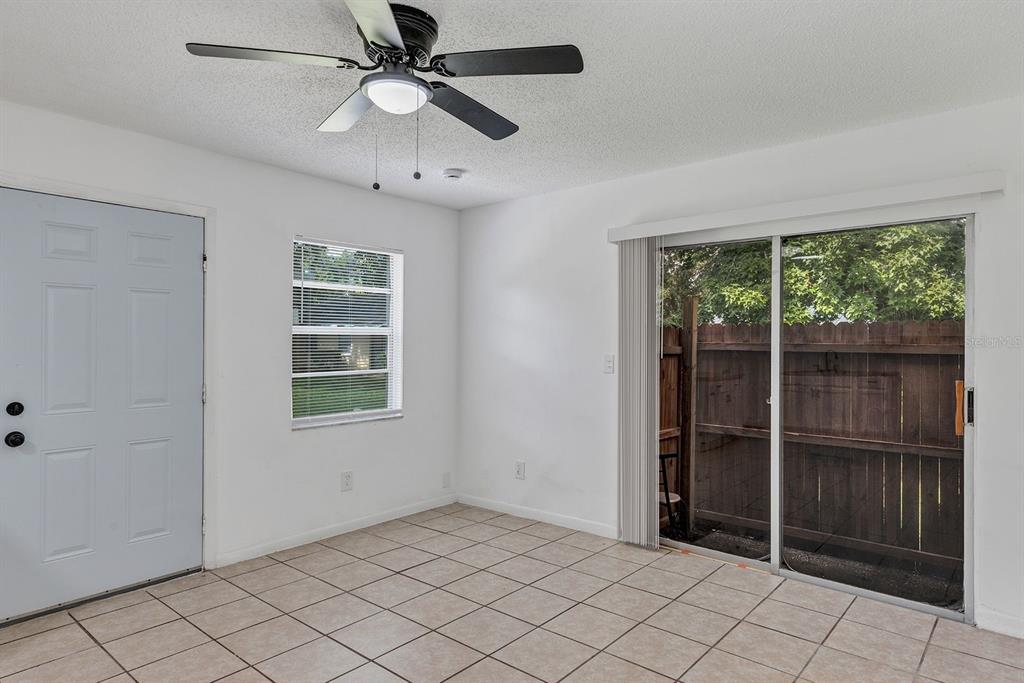 An empty room features white walls, tile flooring, a ceiling fan, and a sliding glass door — 506 NE 28TH AVENUE UNIT C, OCALA, FL