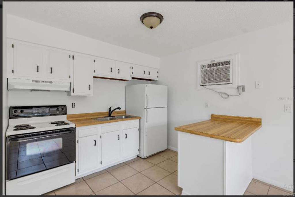 A kitchen with white cabinets, wood-look countertops, white appliances, and a small peninsula — 506 NE 28TH AVENUE UNIT C, OCALA, FL