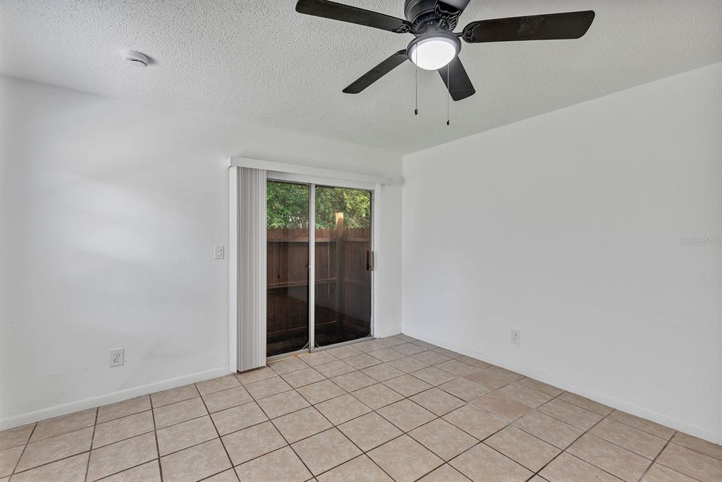 An empty room with beige tile flooring, white walls, a ceiling fan, and sliding glass doors — 506 NE 28TH AVENUE UNIT C, OCALA, FL