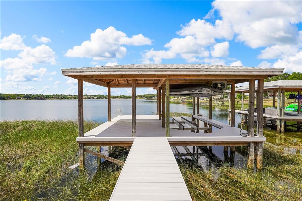 A wooden boat dock with a covered slip extends over a lake with grassy shorelines — 10713 DENALI DRIVE, CLERMONT, FL
