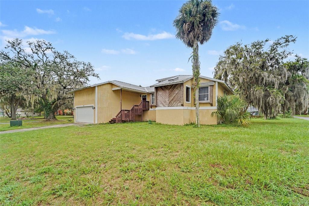 A yellow, single-story house with a garage, wooden stairs, and a tall palm tree — 5422 FOLEY SQUARE, NEW PORT RICHEY, FL