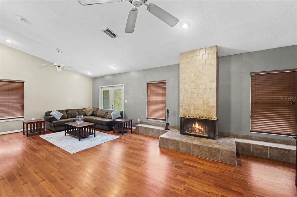 A living room features hardwood floors, a large sectional sofa, and a central tiled fireplace — 5422 FOLEY SQUARE, NEW PORT RICHEY, FL