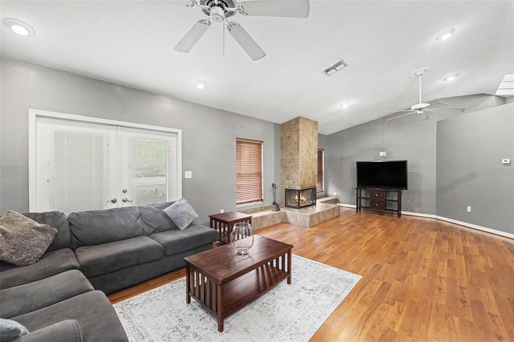 A living room features gray walls, wood flooring, a central tiled fireplace, and a ceiling fan — 5422 FOLEY SQUARE, NEW PORT RICHEY, FL