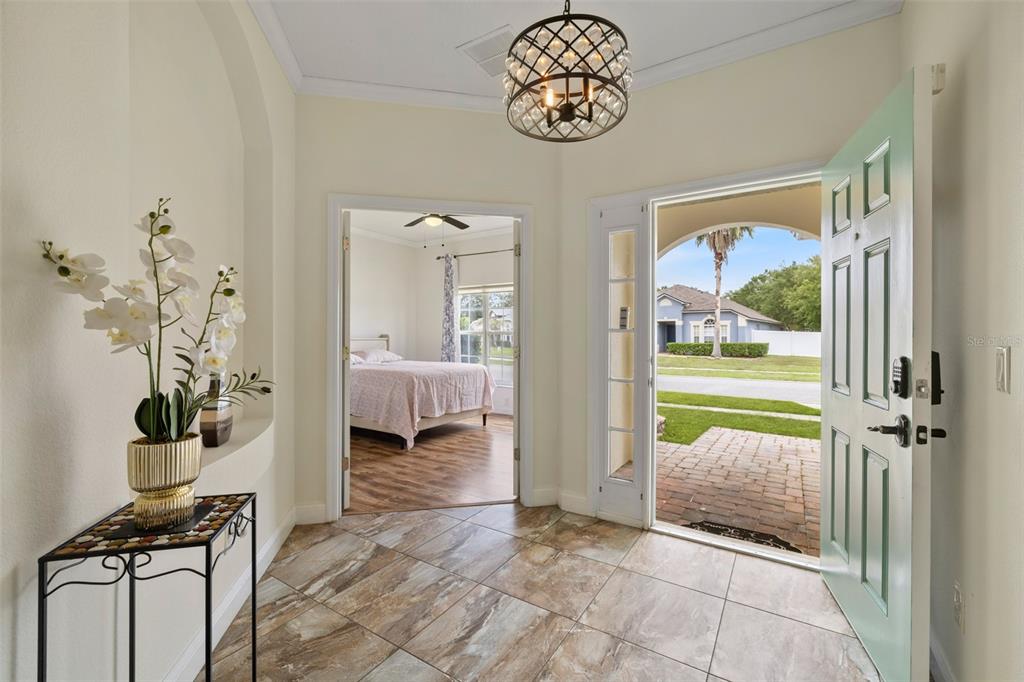 A bright entryway with tiled floors, a decorative light fixture, and a view into a bedroom — 16236 DEER CHASE LOOP, ORLANDO, FL