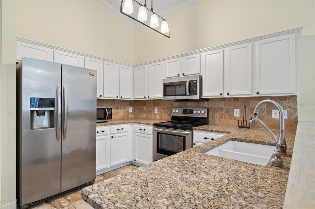 A kitchen features white cabinets, granite countertops, stainless steel appliances, and a tile backsplash — 16236 DEER CHASE LOOP, ORLANDO, FL