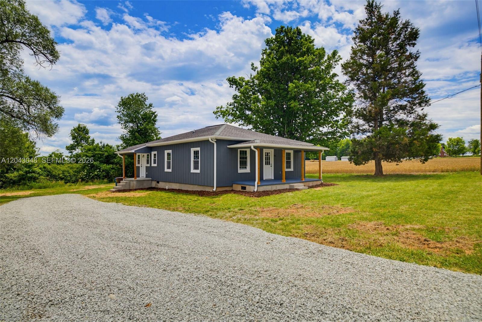 A blue, single-story house with a gravel driveway and a covered porch sits near fields — 7922 Troxler Mill Road, NC 27249, NC